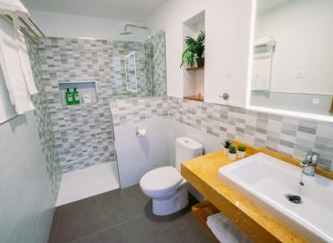 Baño contemporáneo con ducha, lavabo y decoración minimalista, incluyendo productos de higiene personal en estantes.