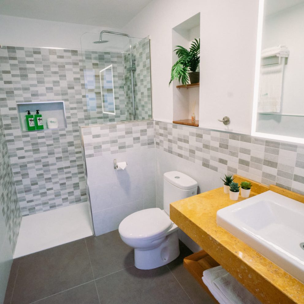 Baño contemporáneo con ducha, lavabo y decoración minimalista, incluyendo productos de higiene personal en estantes.