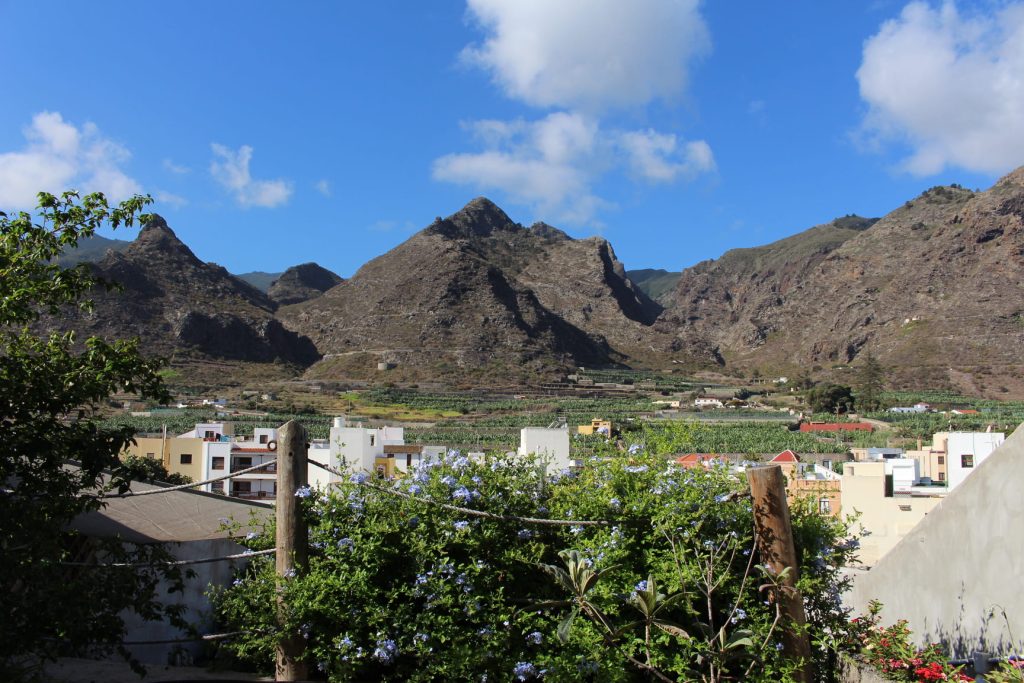 Vista de montañas y vegetación en Tenerife, con casas en primer plano y un cielo azul claro.