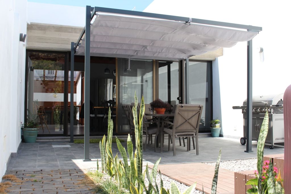 Pérgola de metal con toldo y muebles de patio en un espacio exterior moderno, ideal para reuniones al aire libre y descanso.